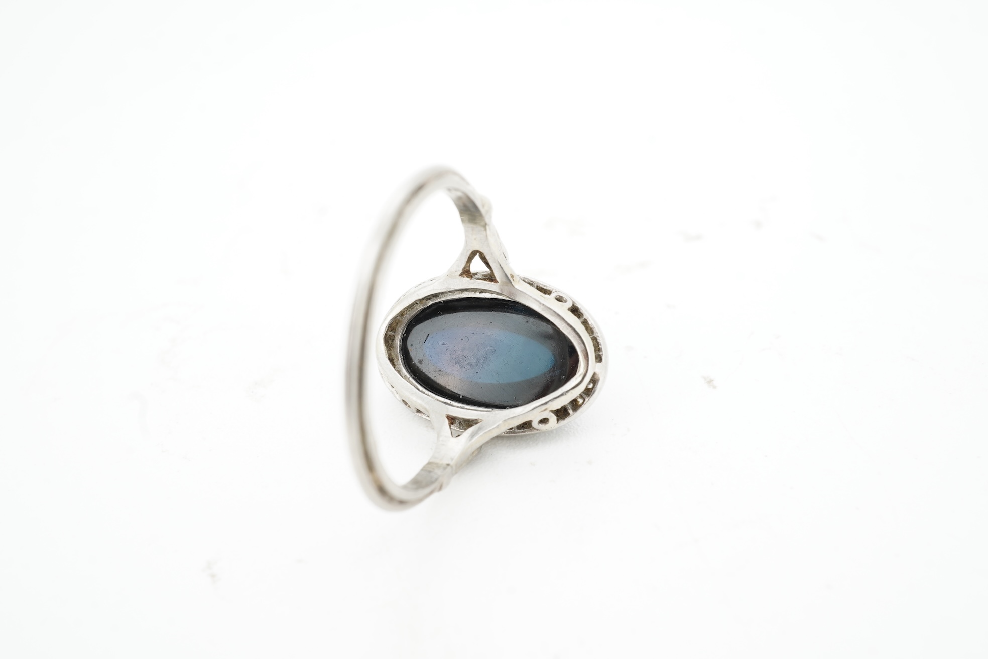 A sapphire and diamond ring, 1920s, set with a cabochon sapphire measuring approximately 2.4 x 6.8 x 4.7mm, within a border of rose-cut diamonds, mounted in platinum, size L1/2